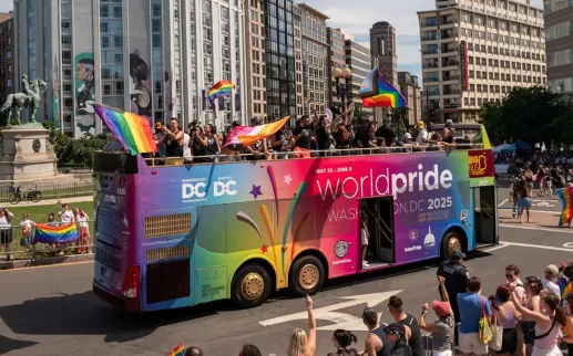 A colorful double-decker bus promoting WorldPride Washington, DC 2025 drives through a lively parade with waving rainbow flags and cheering crowds.
